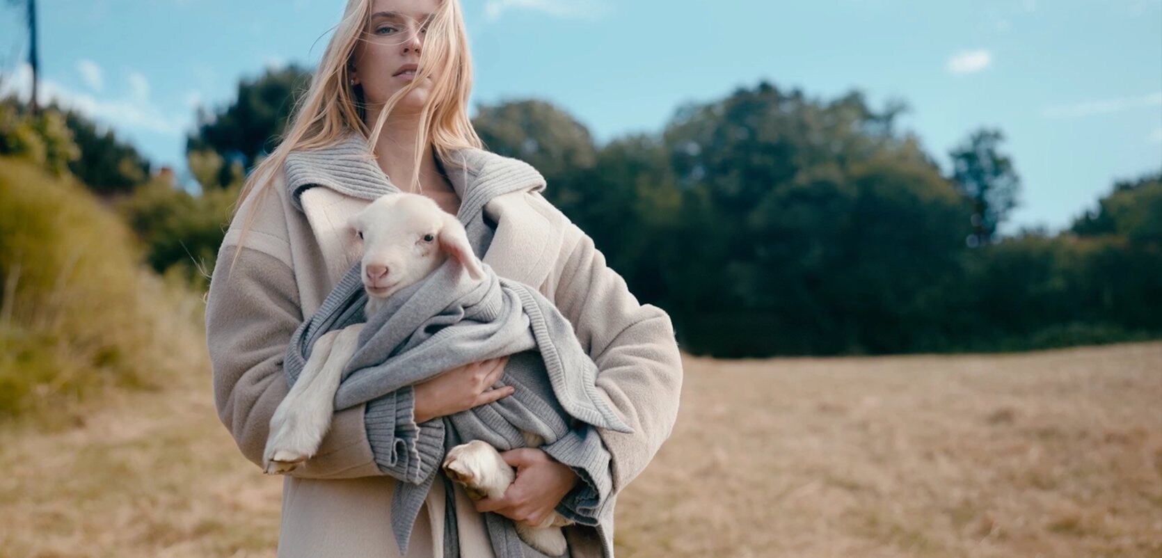 KNITSS FW 26/27 — kollarında kuzu taşıyan, bej kaban ve gri triko giymiş kadın